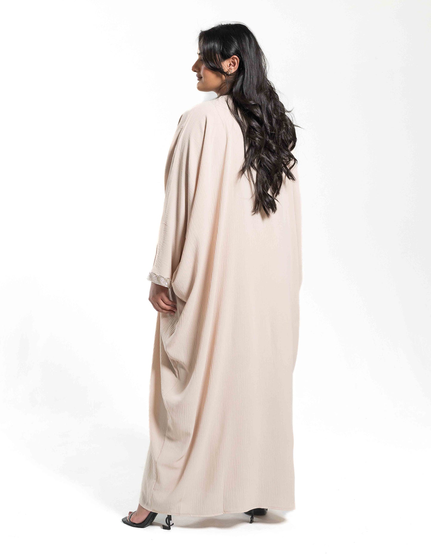 A woman wearing a beige batwing abaya showing the full back view with flowing fabric and design details.