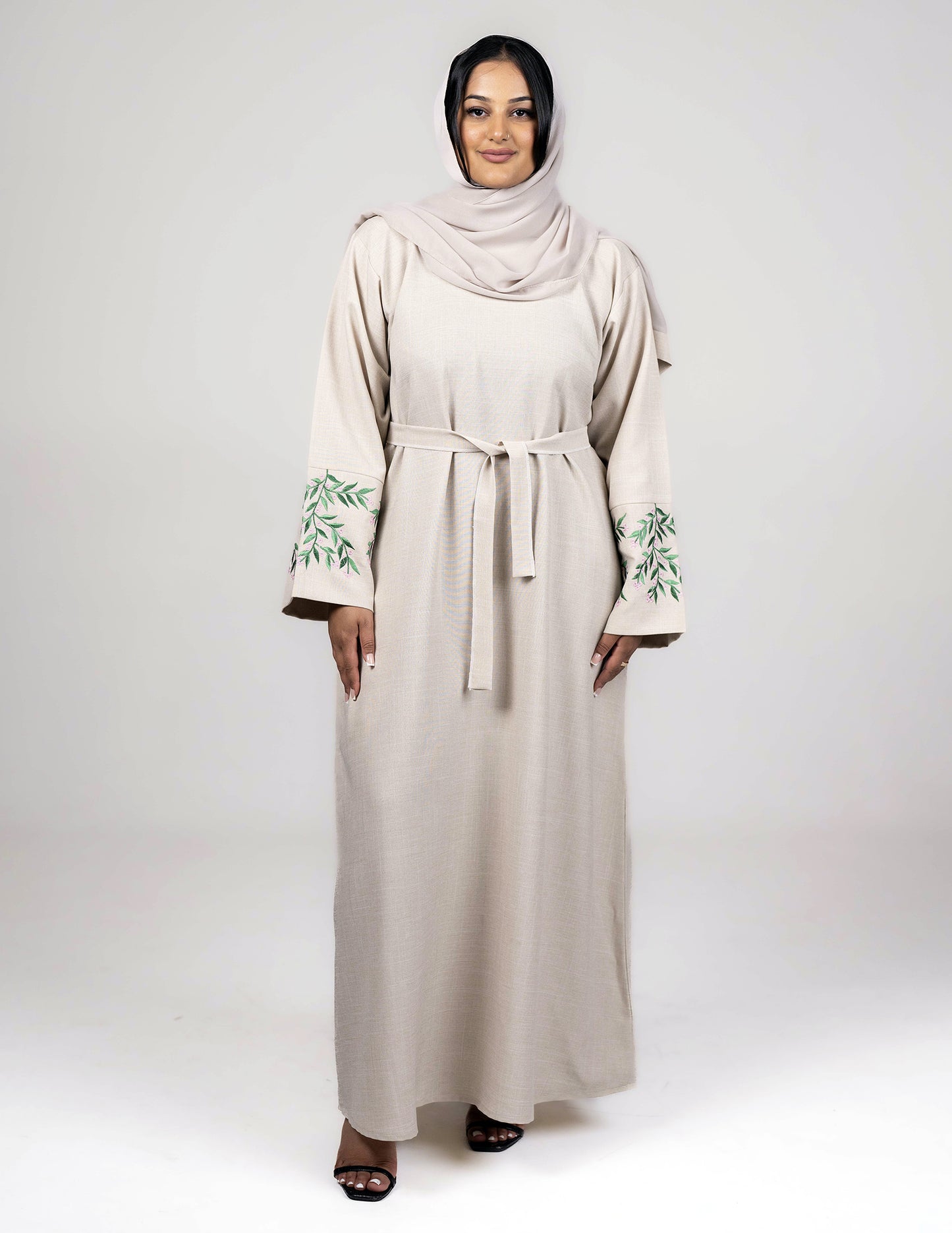 A beige linen abaya with sleeve embroidery, accompanied by a matching belt and hijab.