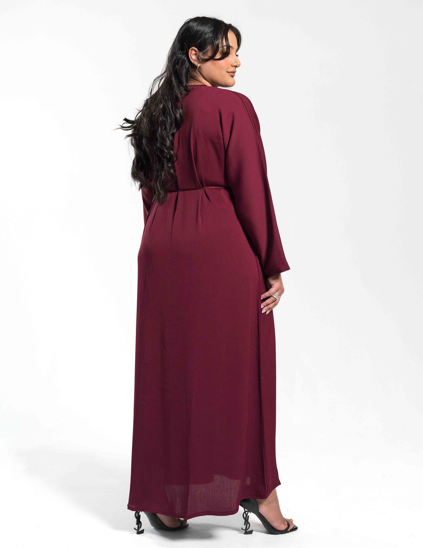 A woman wearing a burgundy abaya showing the full back view with flowing fabric and design details.