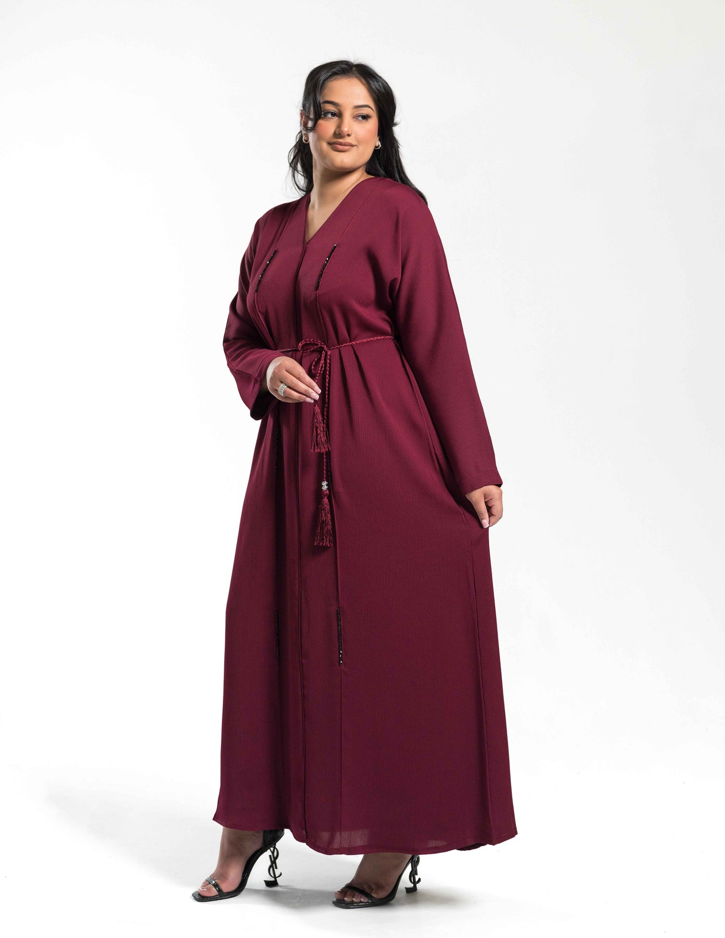 A woman wearing a burgundy abaya holding the front fabric on the left side, showing drape and design details.