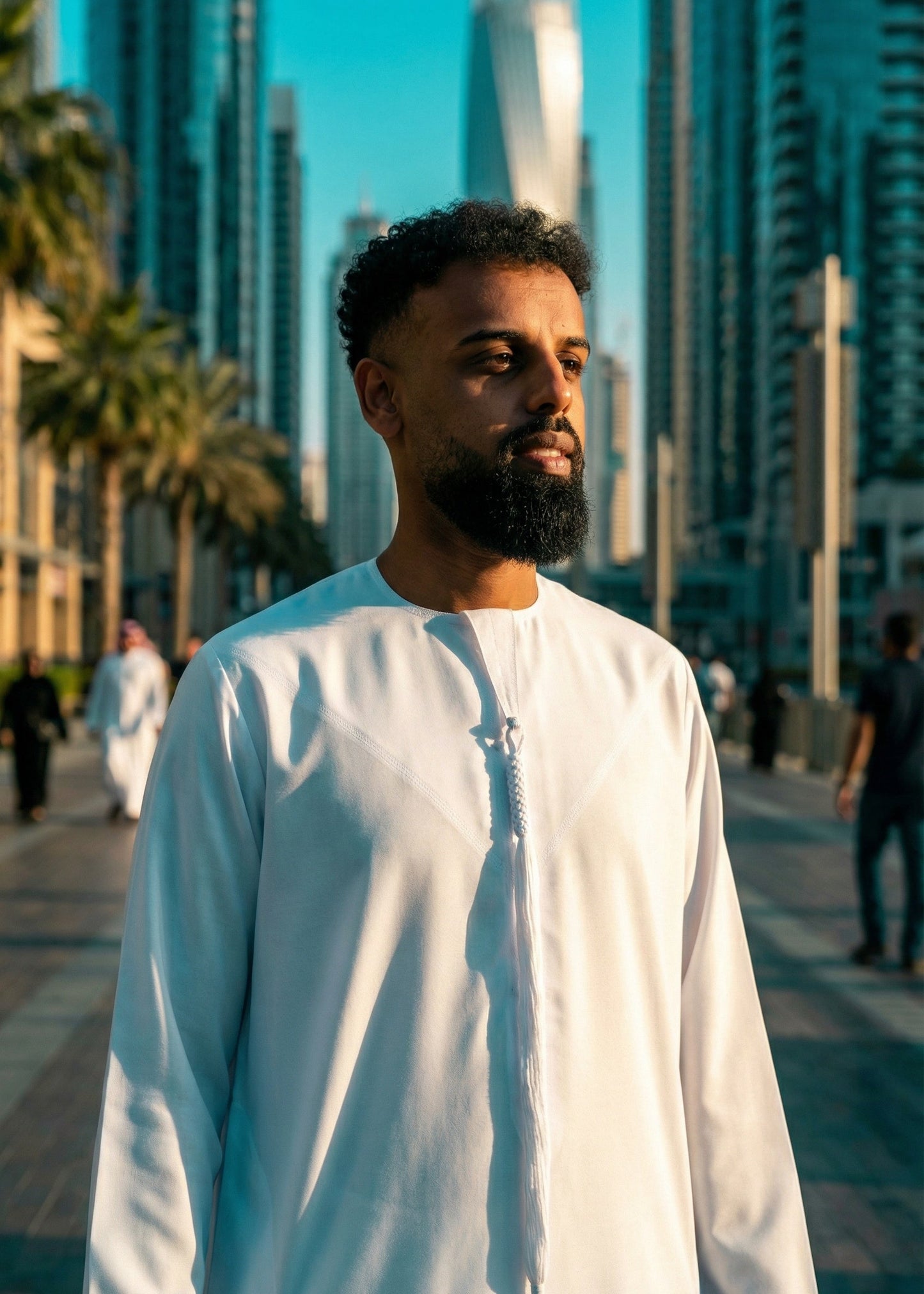 Man in a white traditional outfit standing in front of modern skyscrapers.