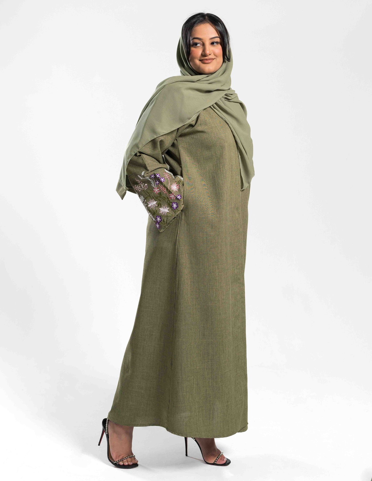 A woman wearing a green linen open abaya with sleeve embroidery and a matching hijab.