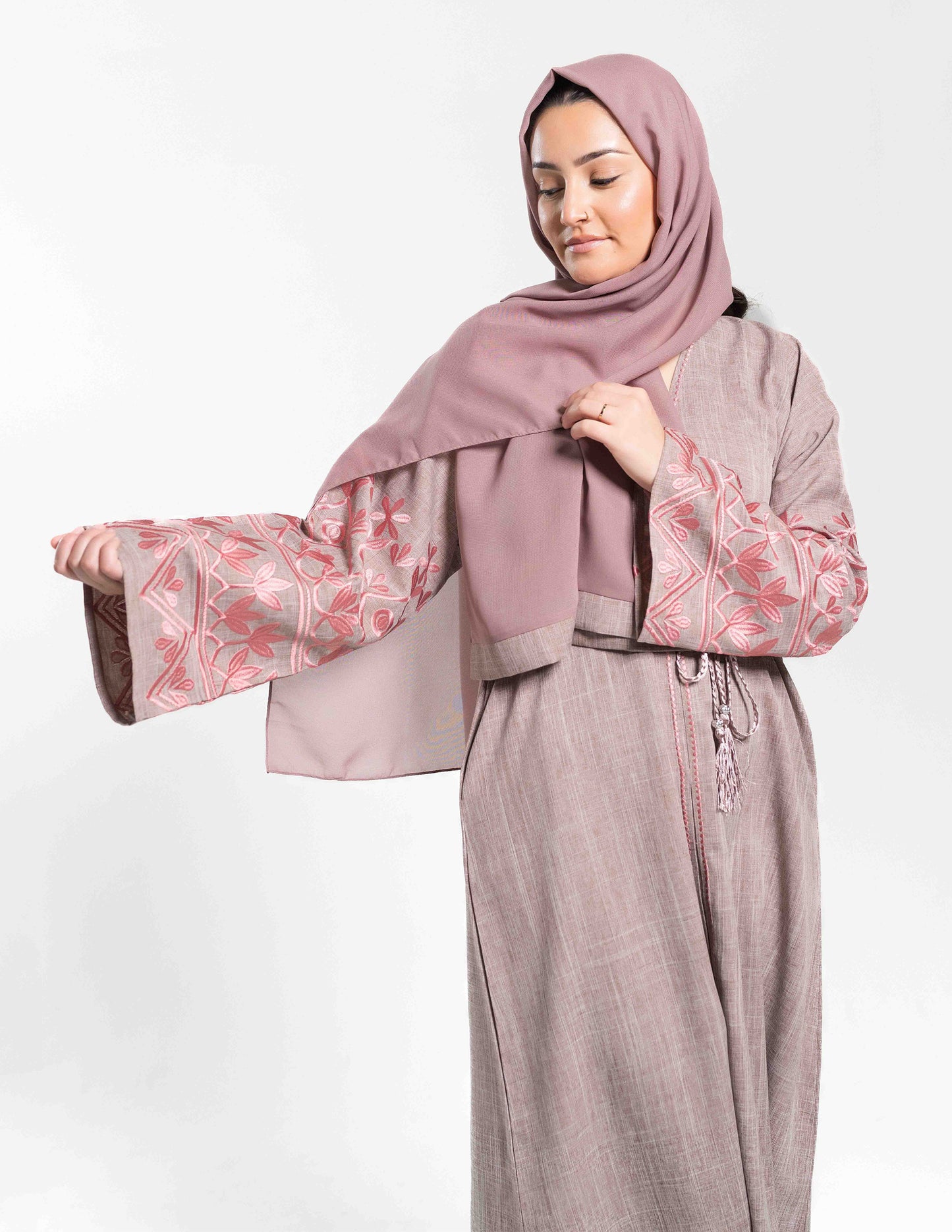 A woman wearing a pink linen Naymaa abaya showing sleeve details, paired with a matching hijab.