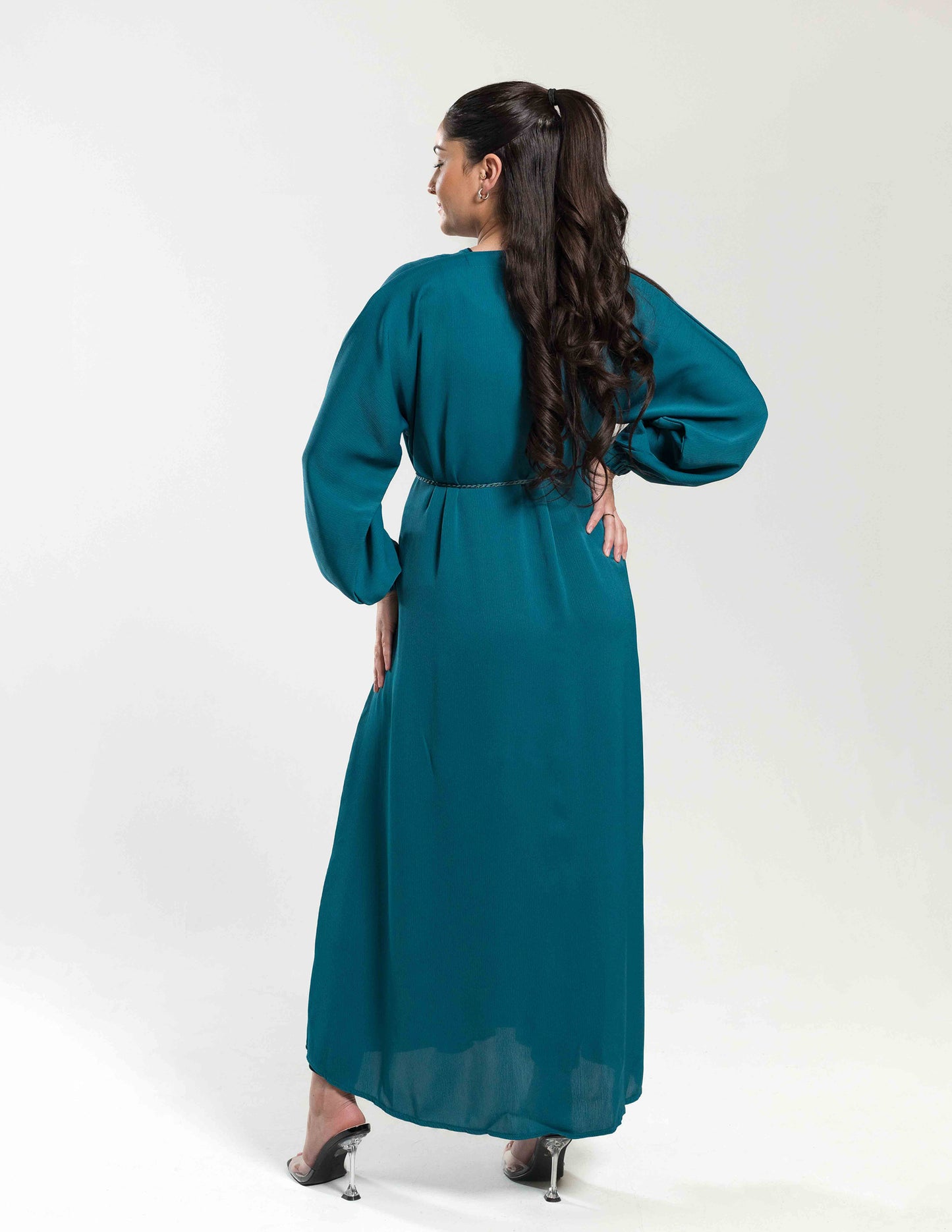 A woman wearing a teal essential abaya showing the full back view with flowing fabric and design details.