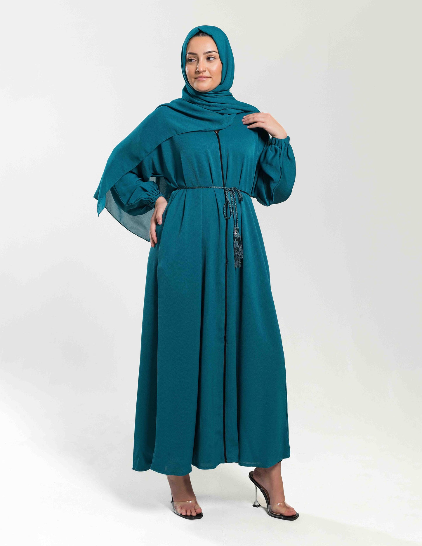 A woman wearing a teal essential abaya paired with a matching hijab, showing the full front view and flowing fabric details.